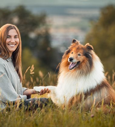 Hundetrainerin und Hund sitzen auf einem Berg und schauen in die Kamera